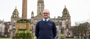 man smiling infront of glasgow city chambers